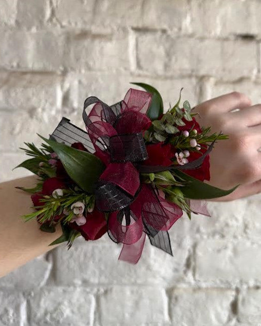 Floral wrist corsage with red flowers and ribbons on a white brick wall background.