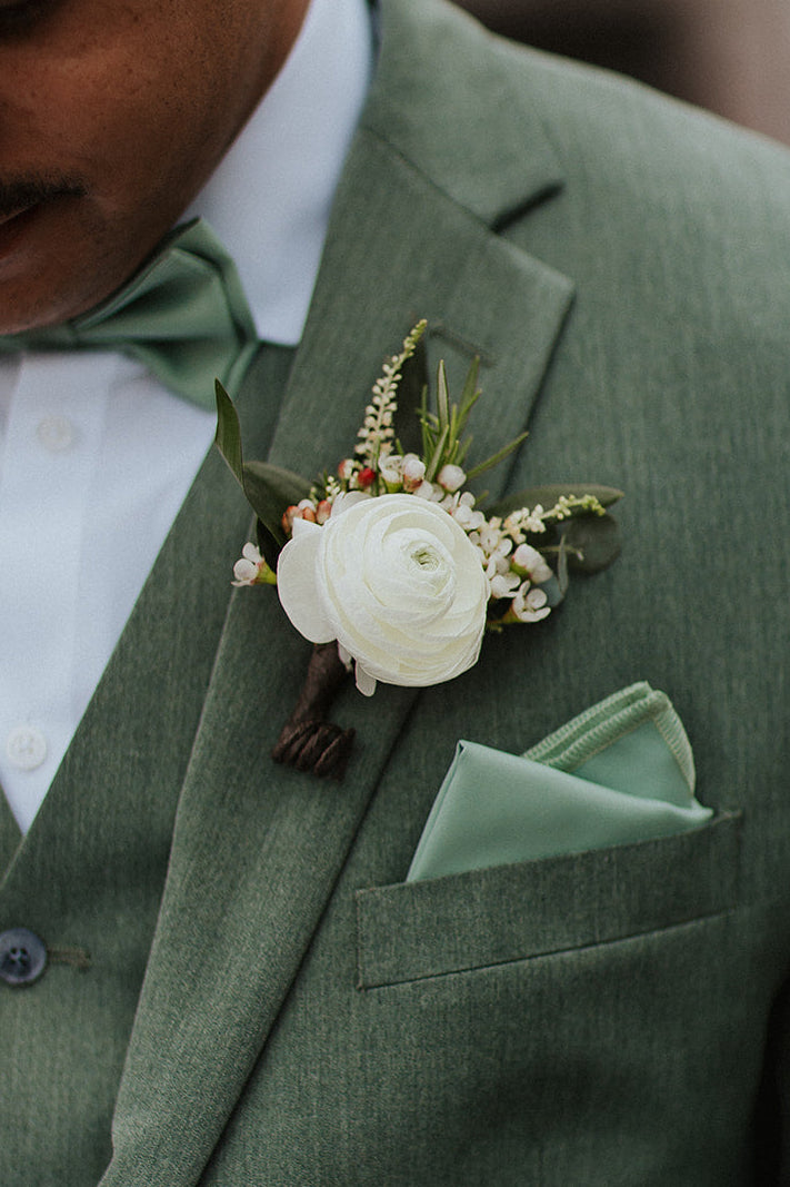 Man wearing a green suit with a ranunculus floral boutonniere and pocket square.