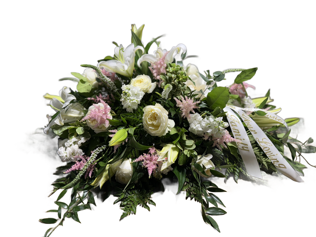 a casket spray arrangement with white lilies and roses, pink astilbe, and other white flowers with a bow and ribbons 