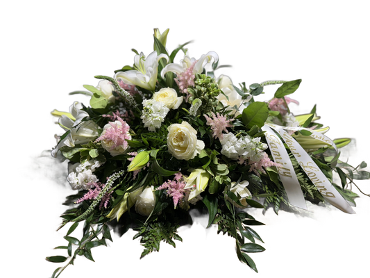 a casket spray arrangement with white lilies and roses, pink astilbe, and other white flowers with a bow and ribbons 