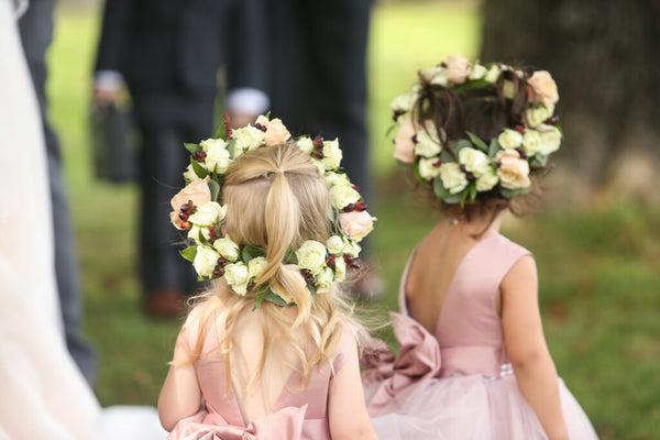 Two young girls in pink dresses with floral headpieces standing outdoors.