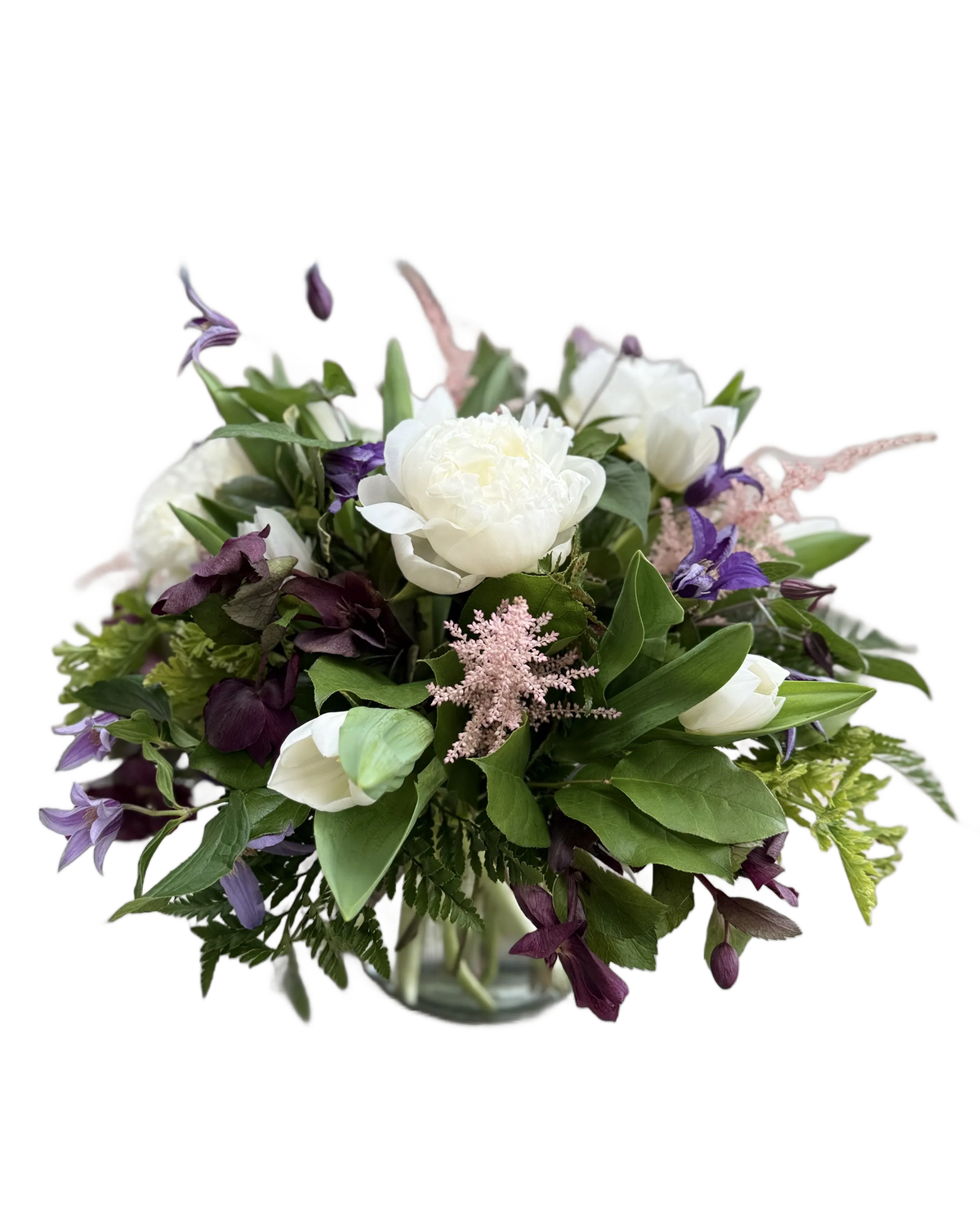 Bouquet of flowers with white peonies, purple clematis, pink astilbe, and other flowers in a clear vase 