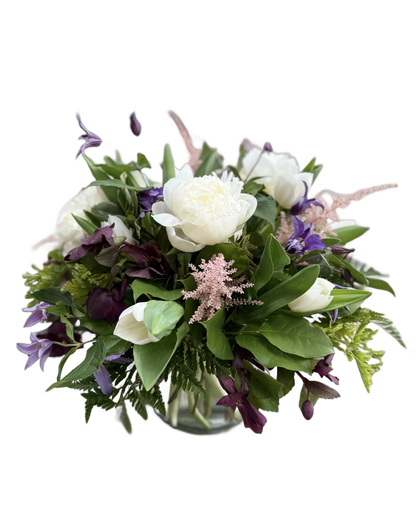Bouquet of flowers with white peonies, purple clematis, pink astilbe, and other flowers in a clear vase 