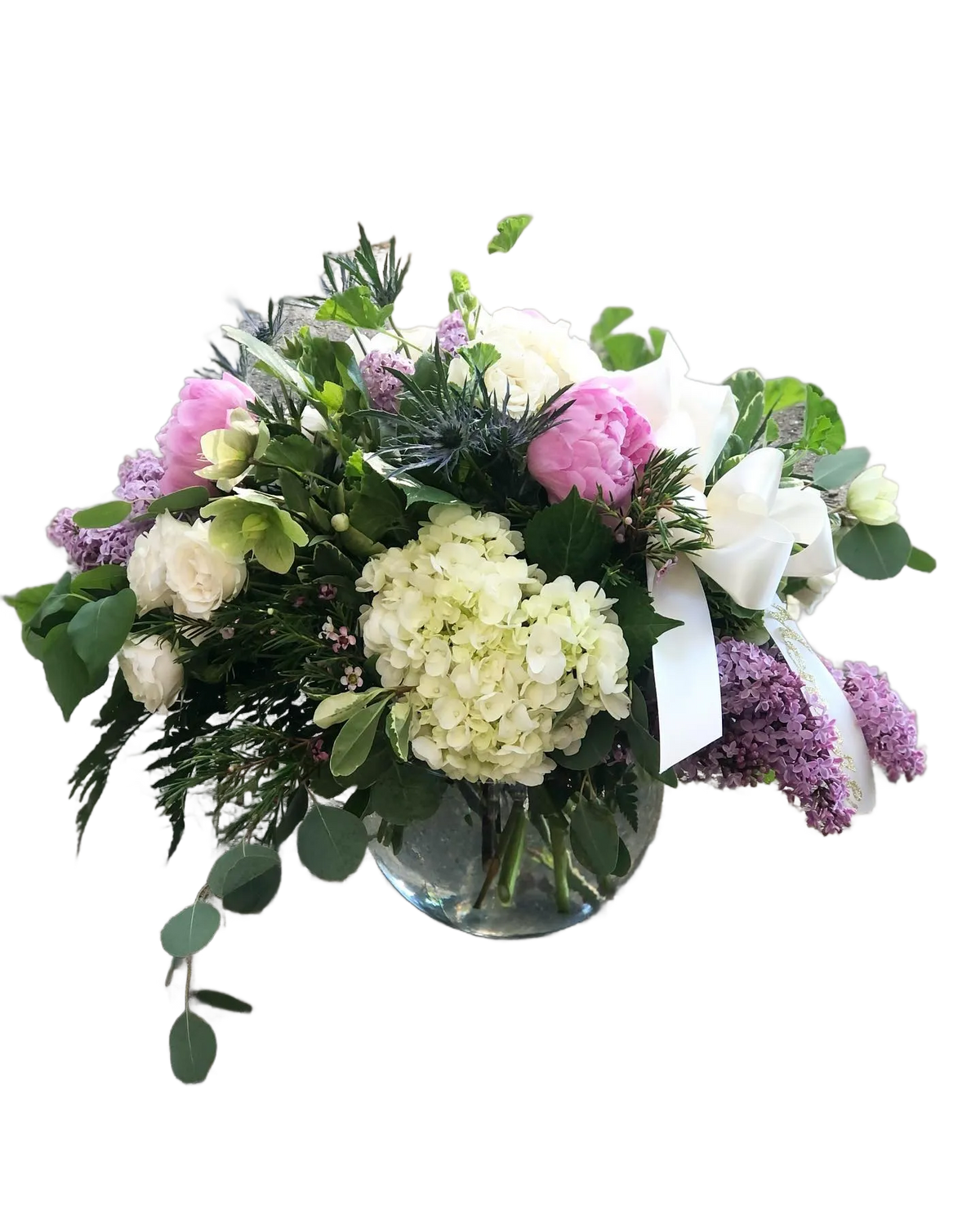 Bouquet of flowers with white spray roses, green hydrangea, pink peonies, and purple lilac with a white bow in a clear vase
