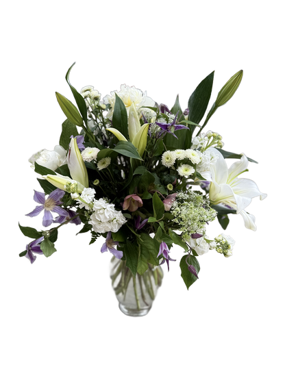 Bouquet of white lilies, purple clematis, and other white flowers in a clear vase