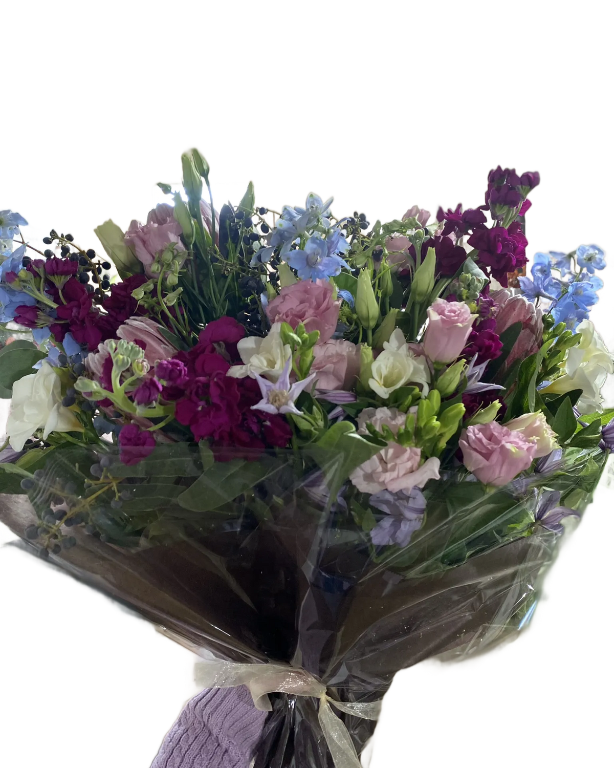 Bouquet of pink, purple, blue, and white flowers wrapped in cellophane and tissue with a white ribbon