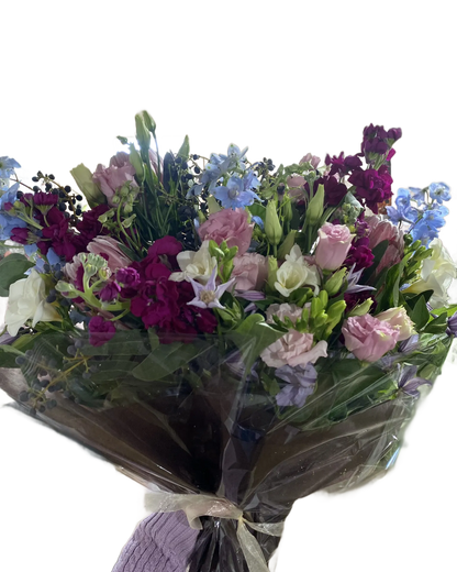 Bouquet of pink, purple, blue, and white flowers wrapped in cellophane and tissue with a white ribbon